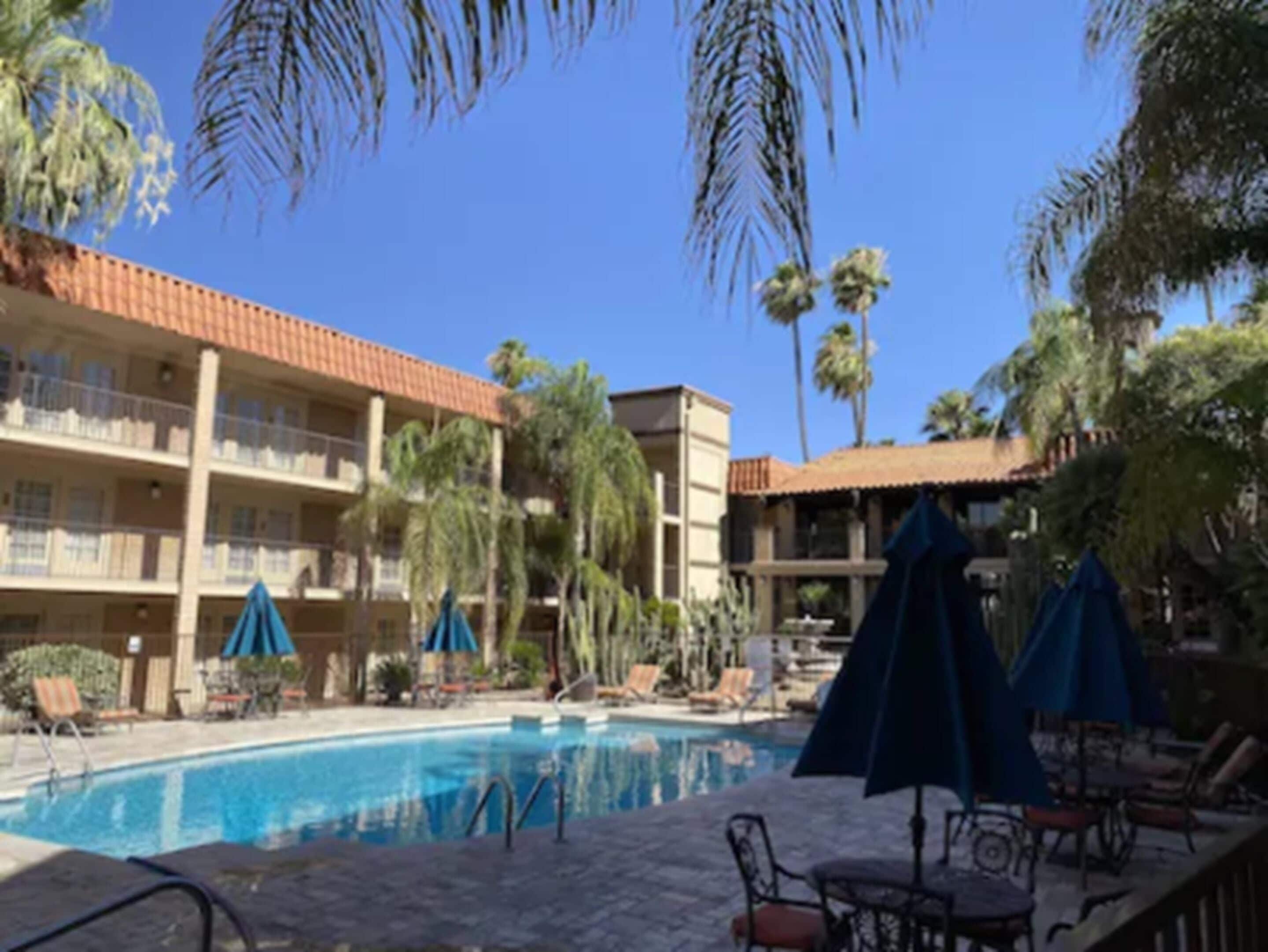 Un hotel con piscina, palmeras y mobiliario exterior.