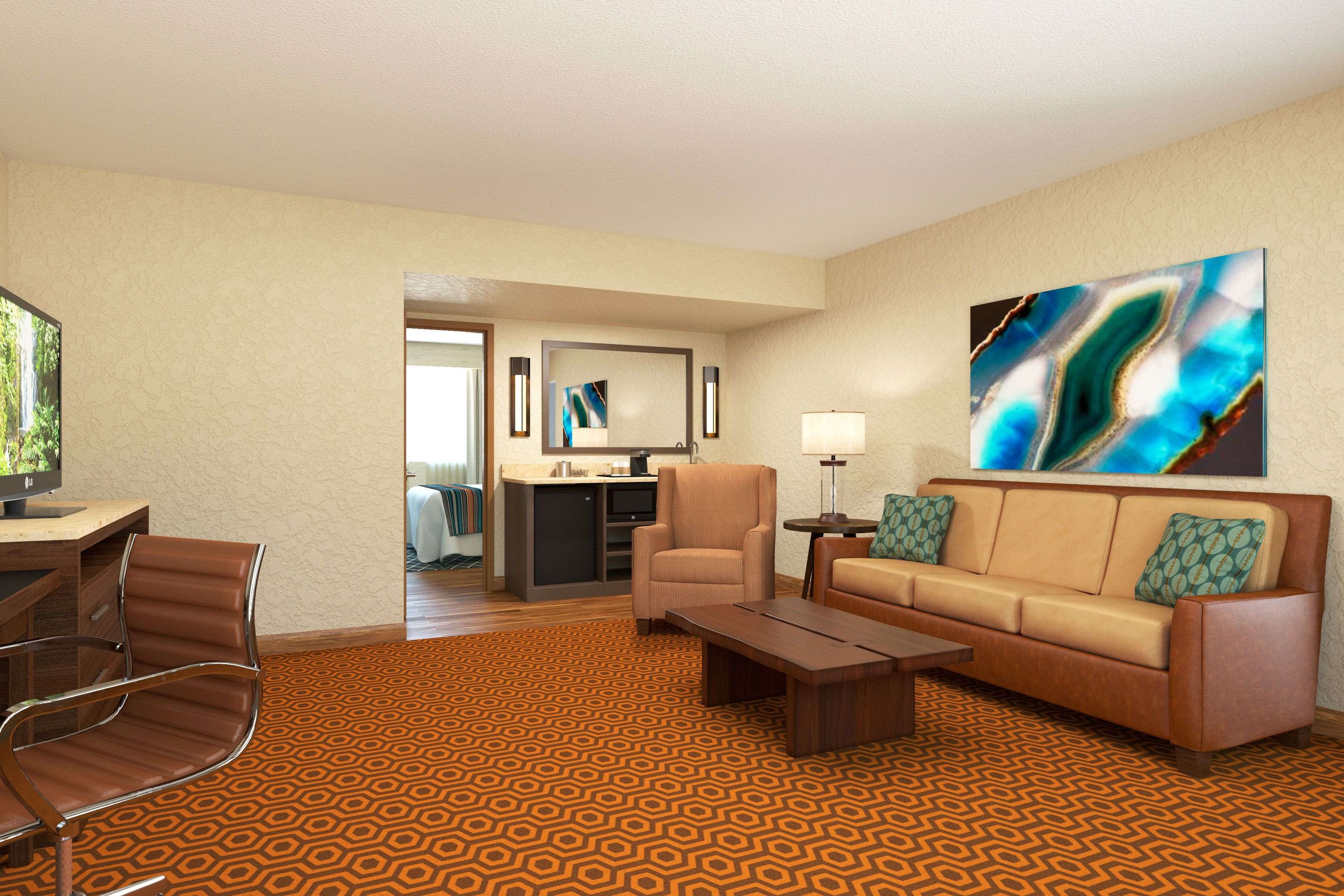 Habitación de hotel con sofá, sillón, mesa de centro y televisión. Se observa una cocina al fondo.