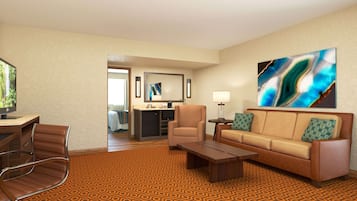 Habitación de hotel con sofá, sillón, mesa de centro y televisión. Se observa una cocina al fondo.