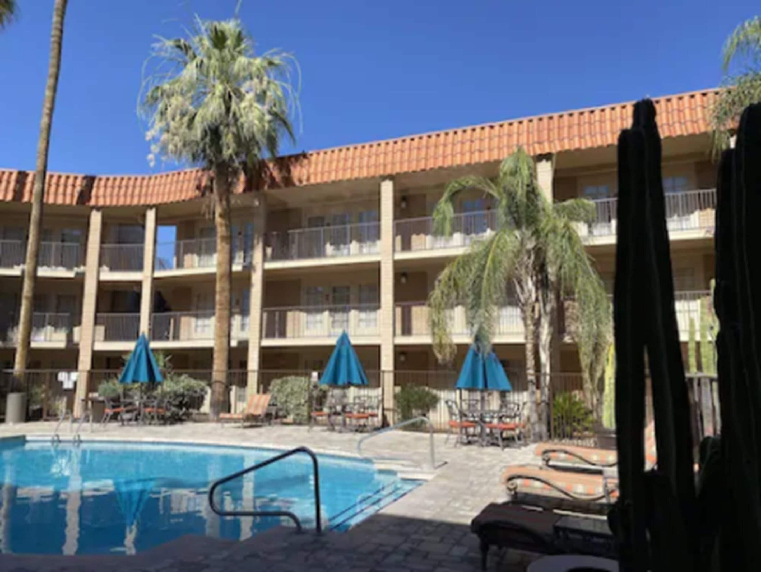 A hotel with a swimming pool, palm trees, and outdoor seating.
