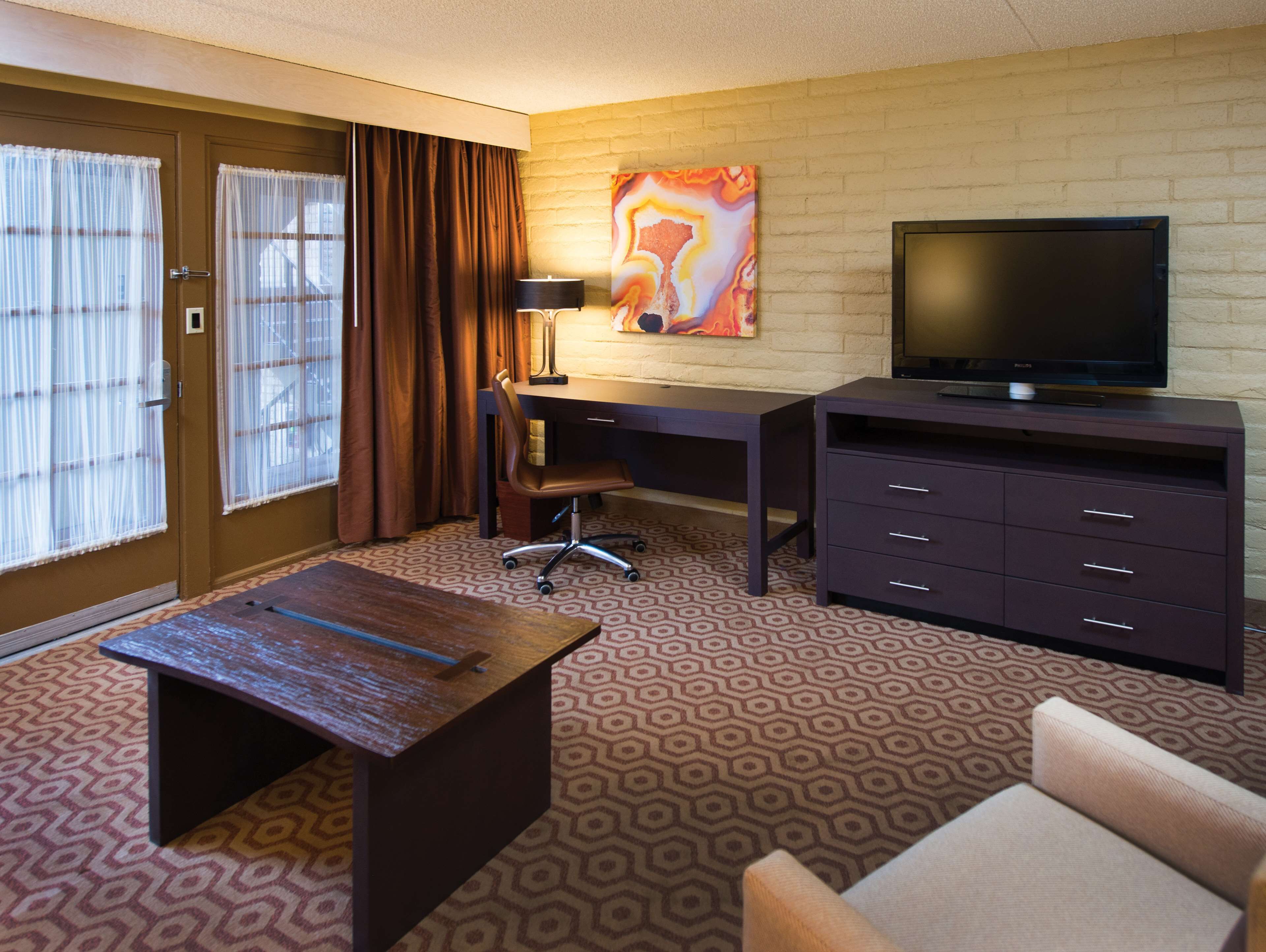 A hotel room with a desk, chair, television, and a small table.