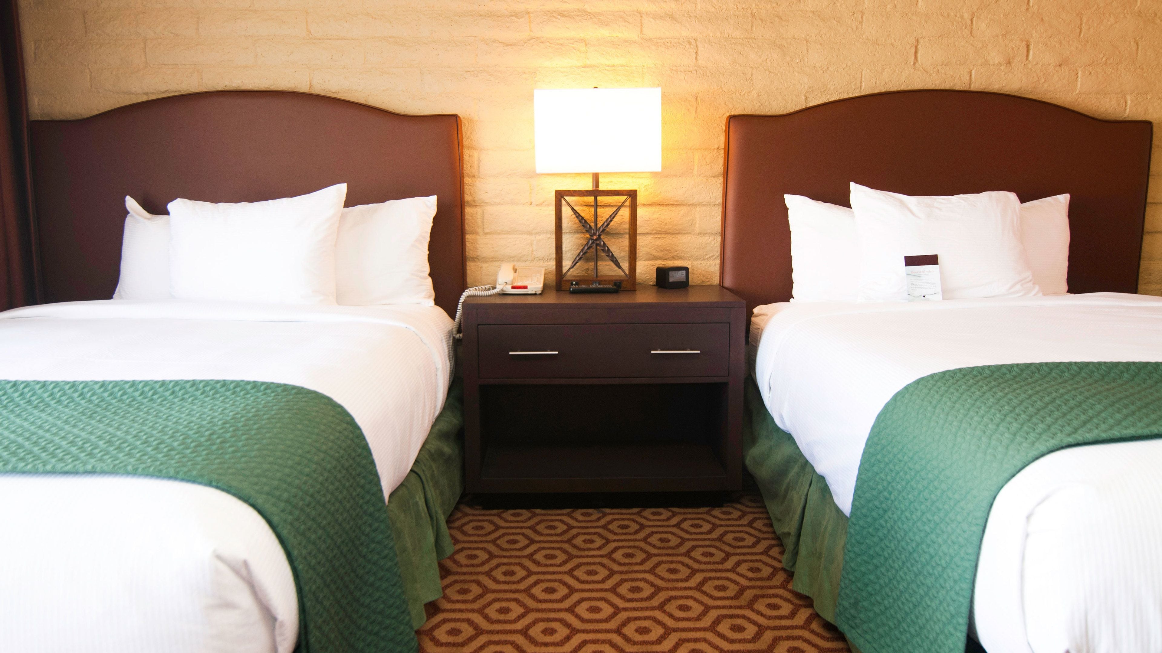 A hotel room with two beds, a nightstand with a lamp, and a patterned carpet.