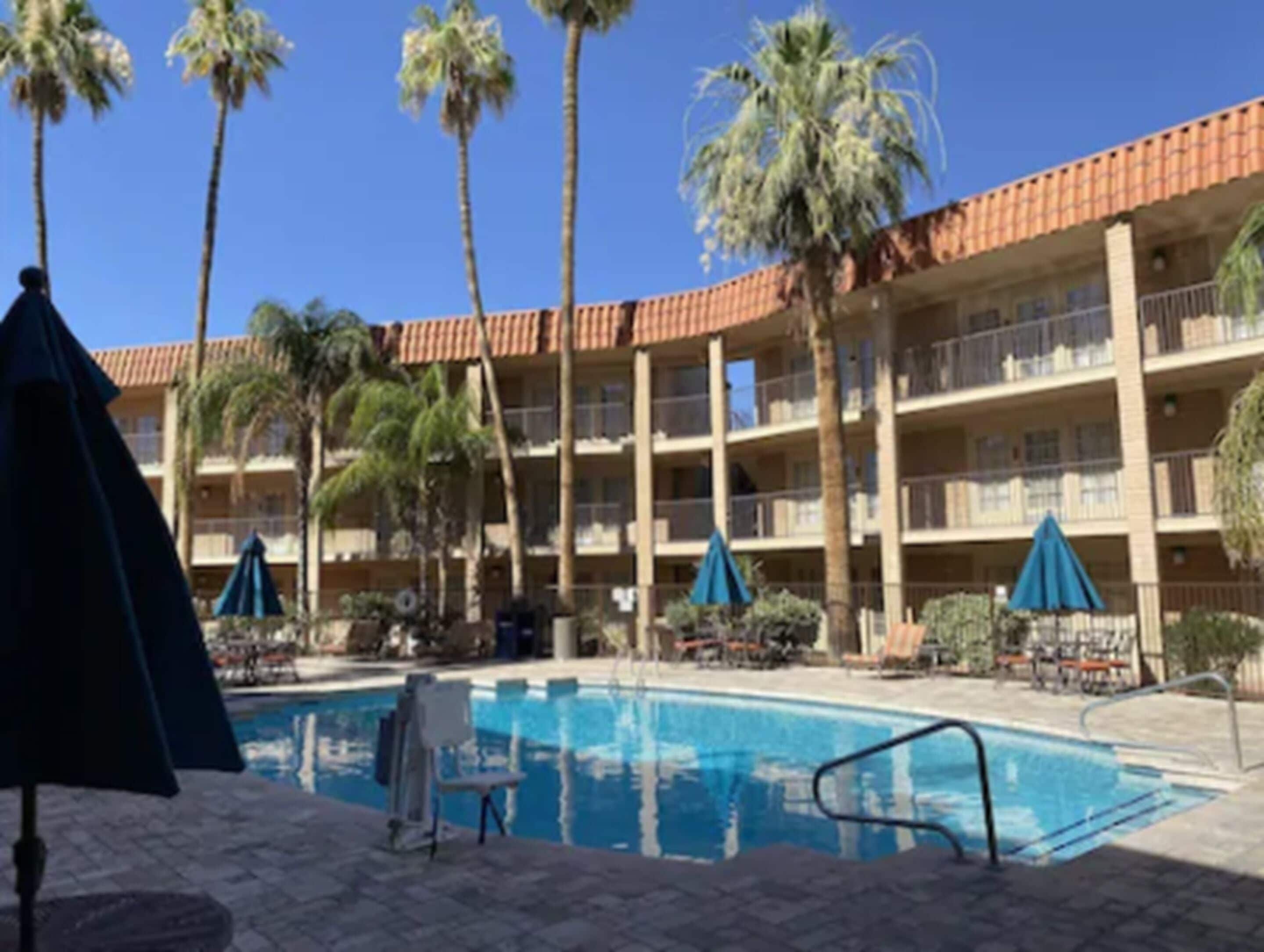 A hotel with a pool, palm trees, and a red-tiled roof.