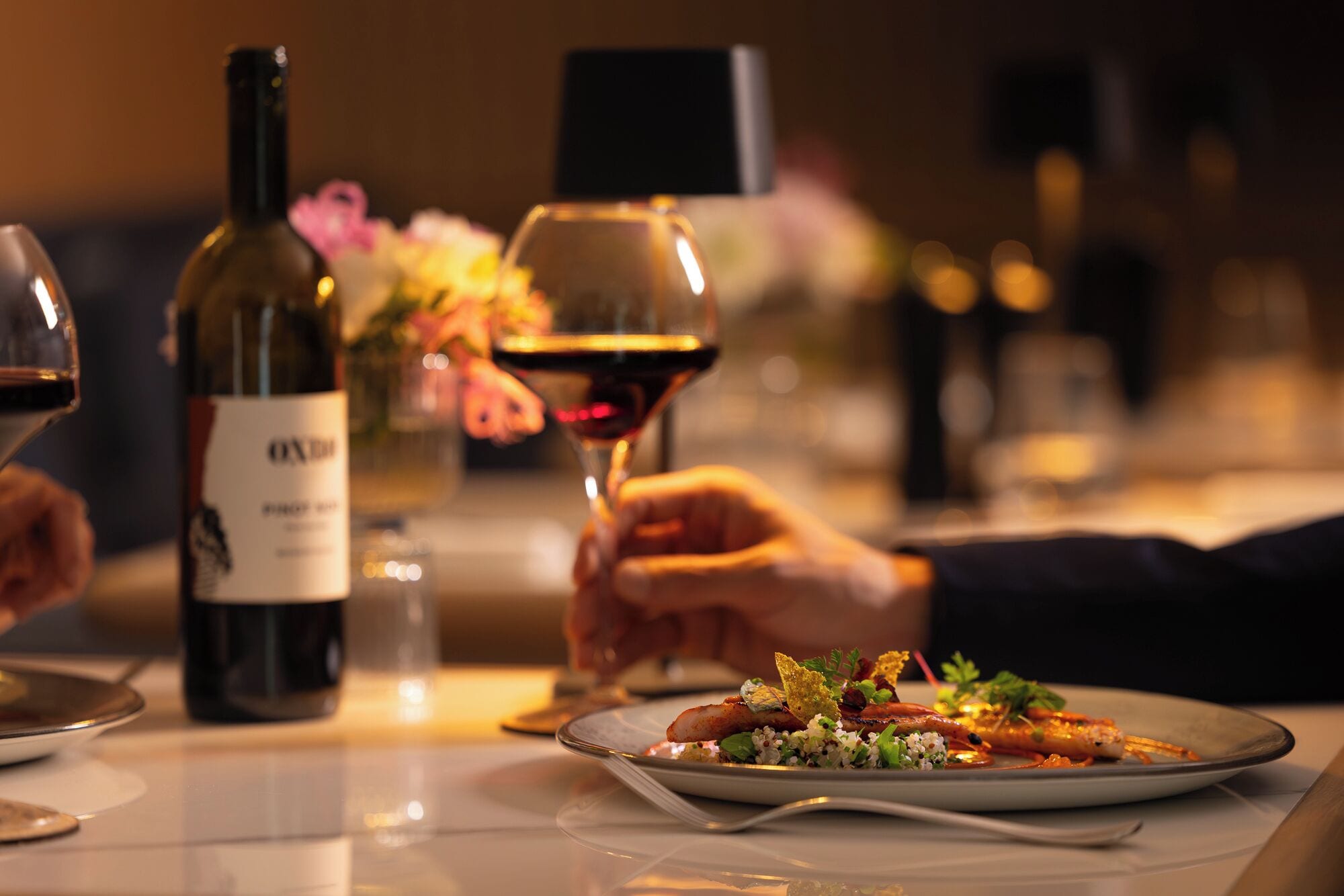 A dining table with a plate of food, a wine bottle, and a glass of wine.
