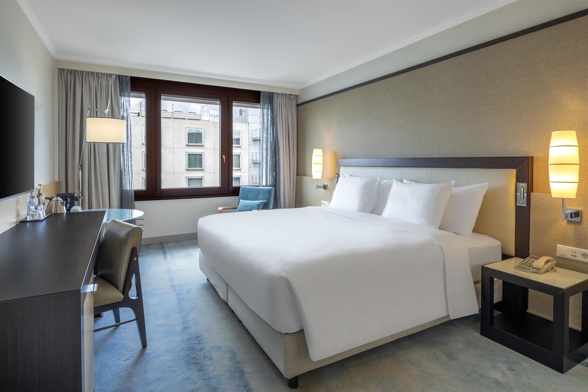 A hotel room with a bed, a desk, a chair, a telephone, and a window with curtains.
