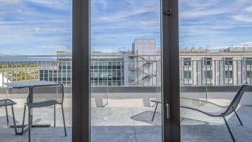 A balcony with a table and chairs, a hammock, and a view of a building and sky.