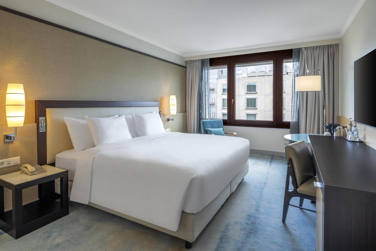 A hotel room with a large bed, bedside lamps, a desk, and a chair.