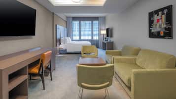 A hotel room with a bed, a desk, a TV, a sofa, and a painting on the wall.