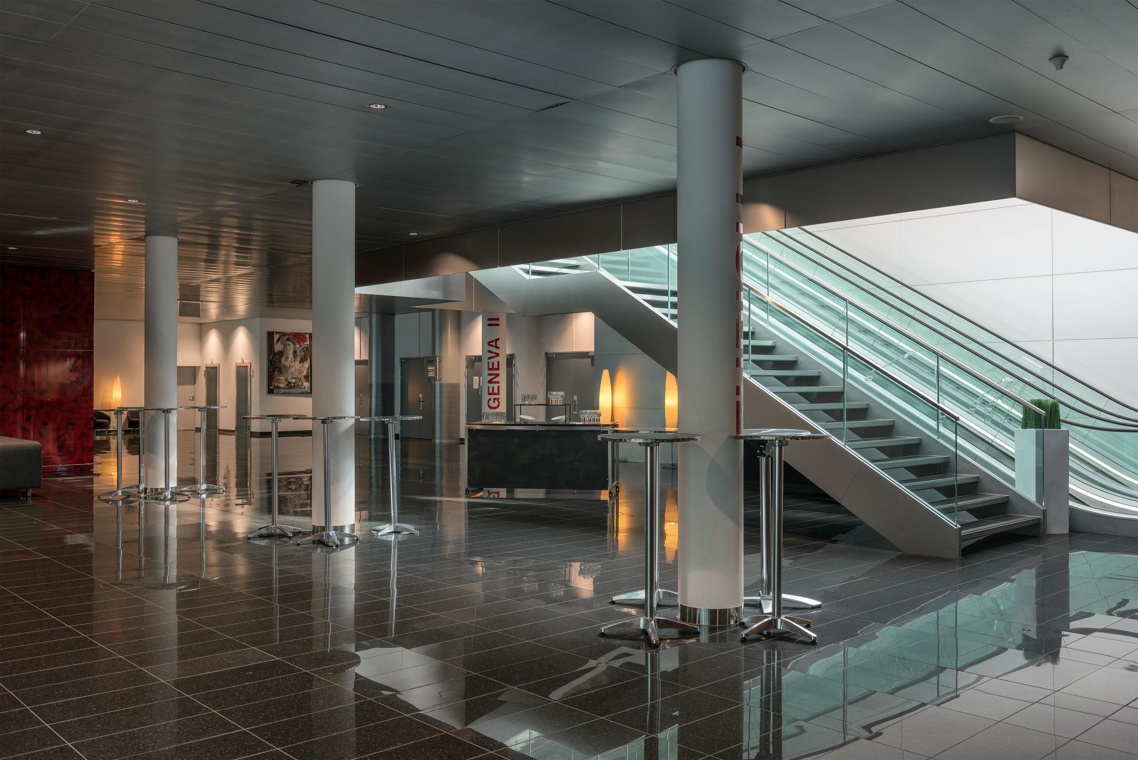 Eine moderne Lobby mit einer Glasstiege, poliertem Boden und einer zentralen Säule mit einem Schild.