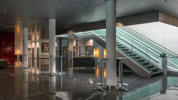 Eine moderne Lobby mit einer Glasstiege, poliertem Boden und einer zentralen Säule mit einem Schild.