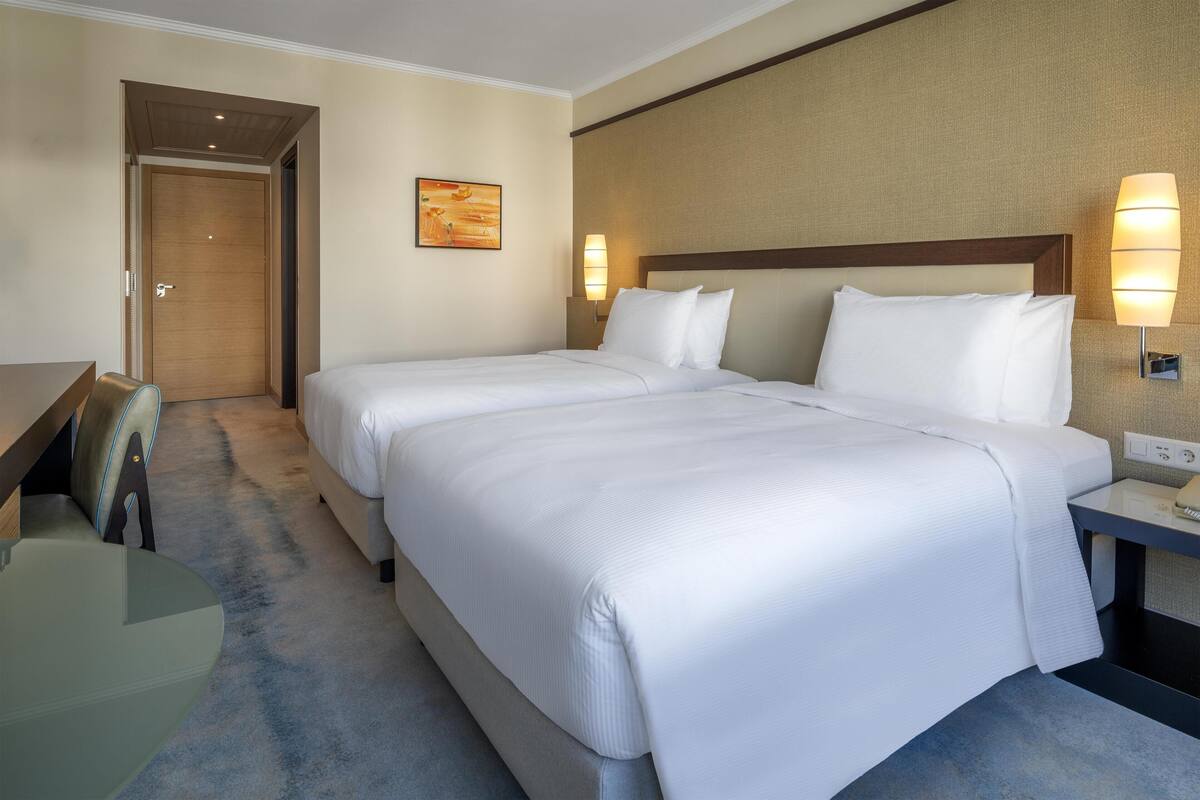 A hotel room with two beds, a desk, and a chair.