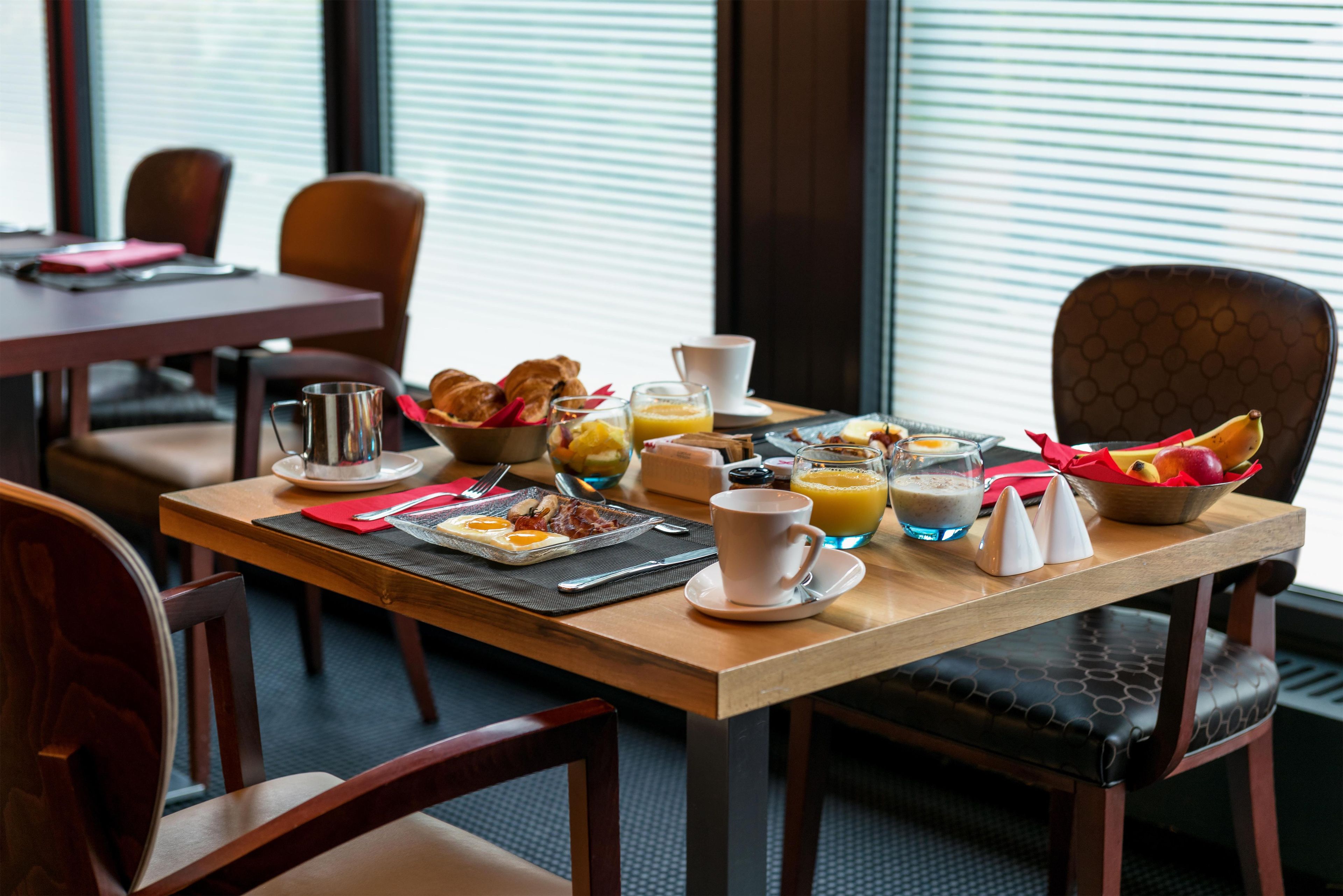 A breakfast setting with a table set for two, including croissants, eggs, bacon, and fruit.