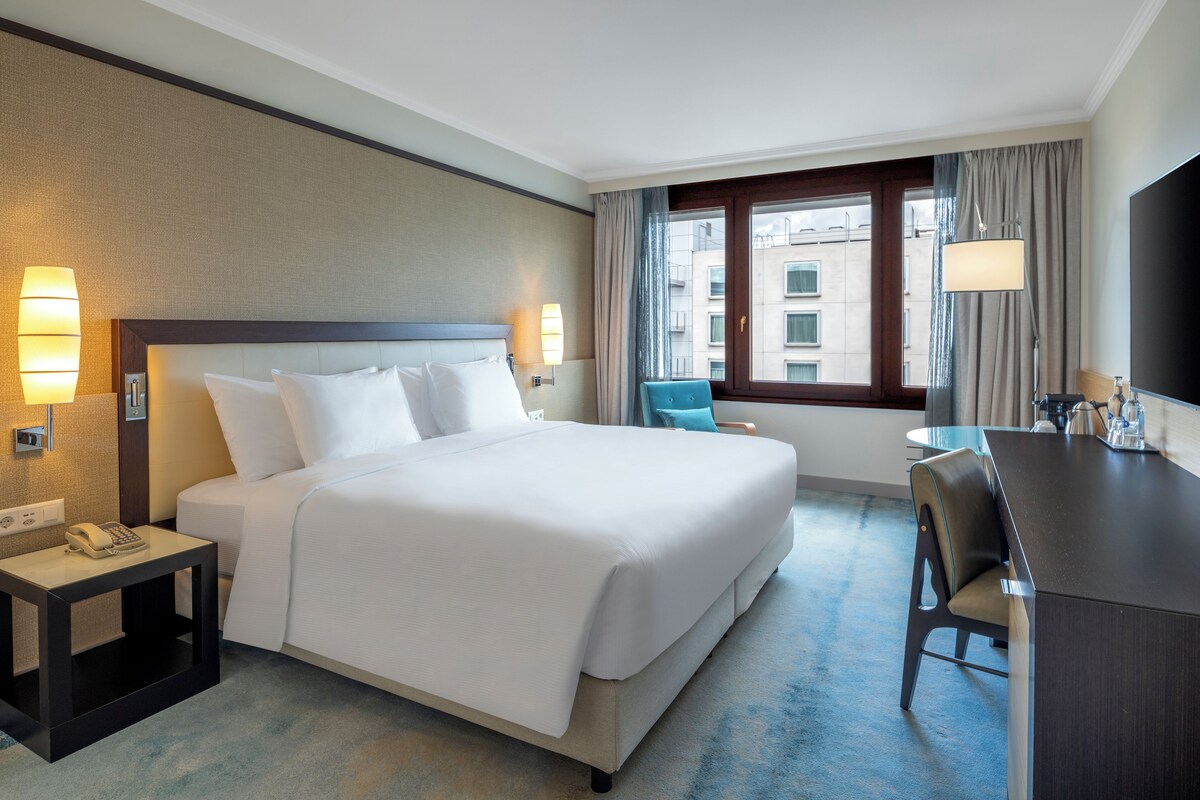 A hotel room with a large bed, bedside lamps, a desk, and a chair.