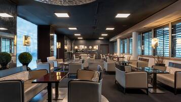A modern hotel lobby with seating areas, a reception desk, and large windows.