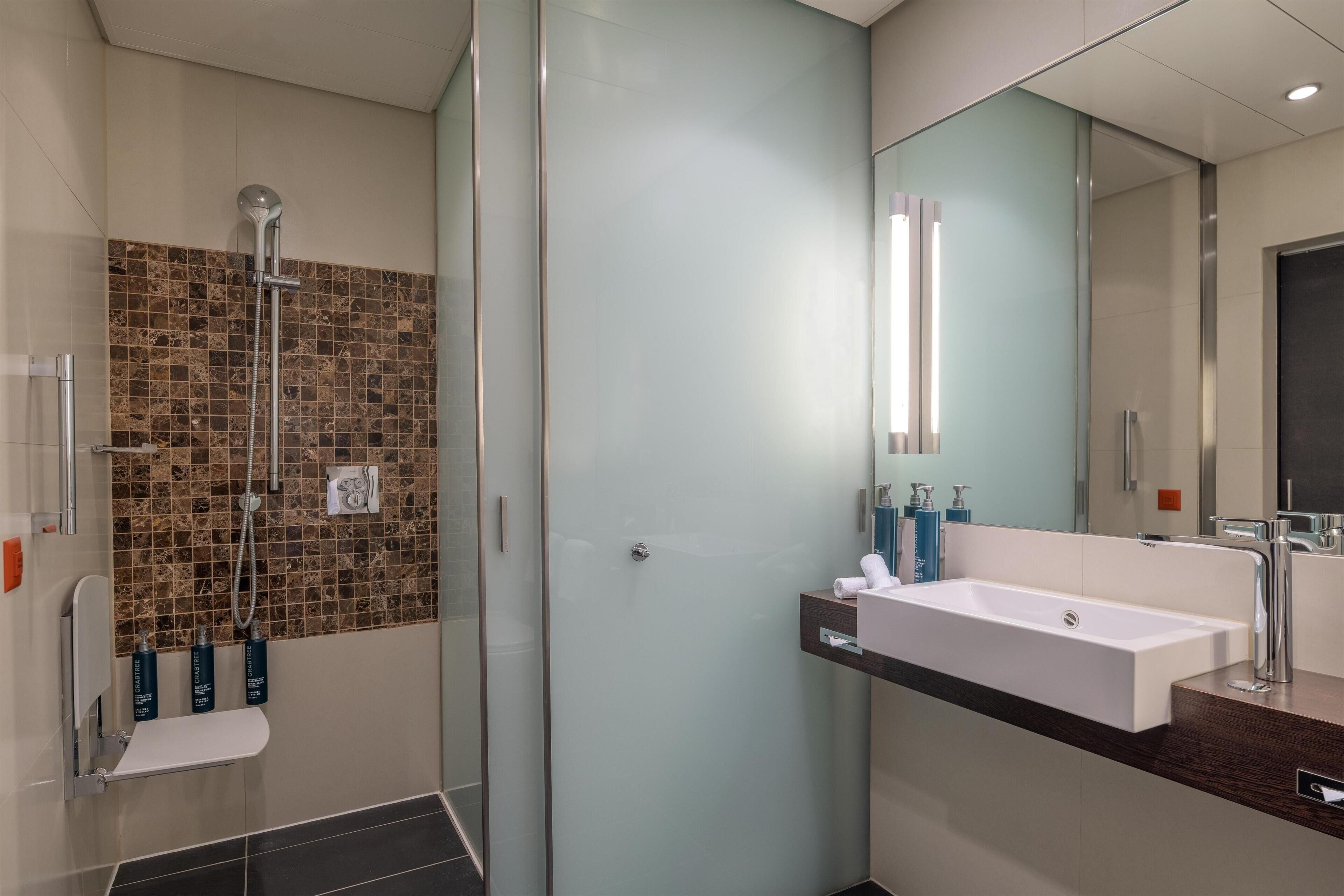 A modern bathroom with a glass shower enclosure, a white sink, and a mirror.