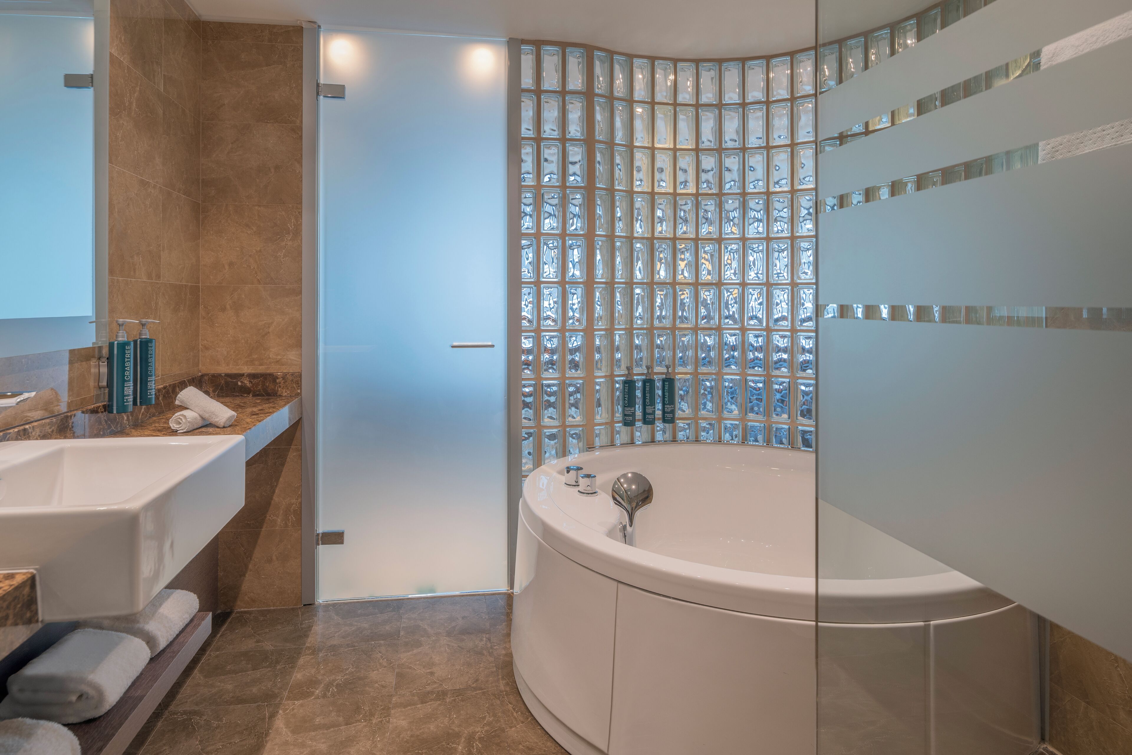 Une salle de bain moderne avec une grande baignoire, une paroi en verre et un meuble-lavabo avec des articles de toilette.
