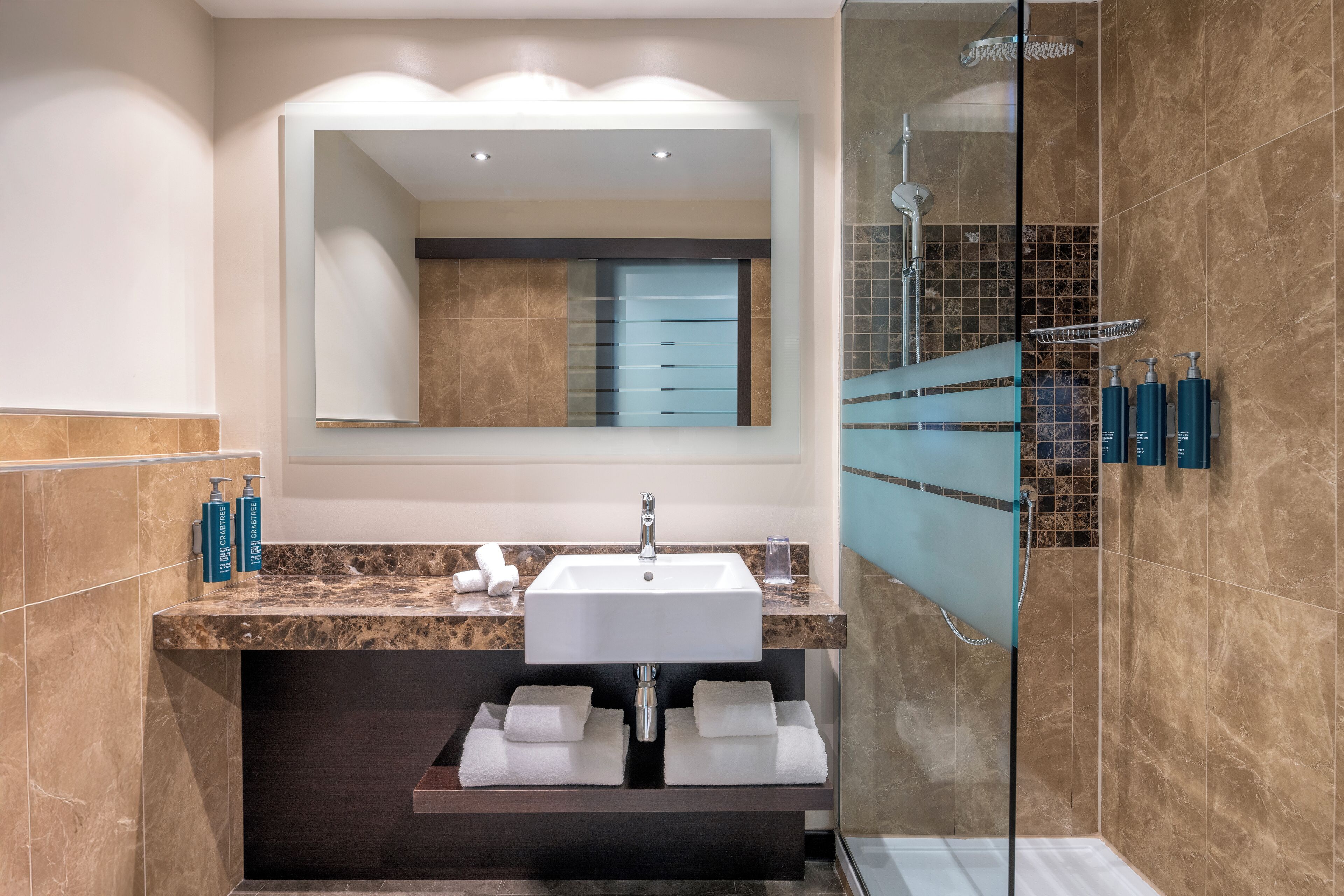 Une salle de bain moderne avec un lavabo en marbre, un grand miroir et une douche à parois de verre.