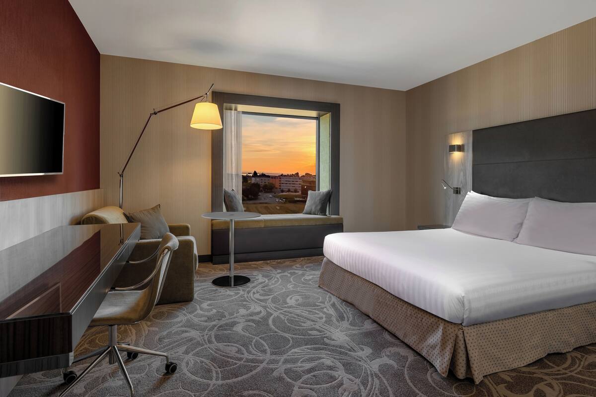 A hotel room with a bed, desk, chair, and a window with a view.