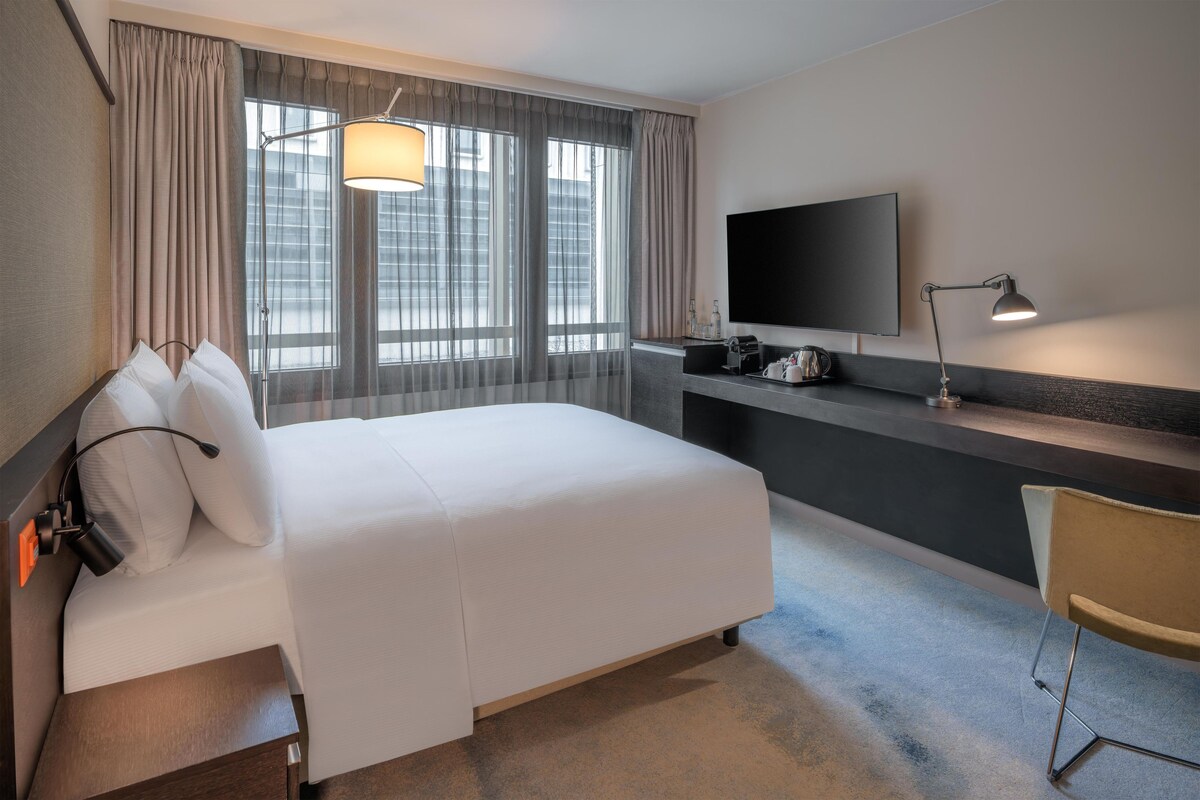 A hotel room with a bed, a desk, a television, and a window with curtains.