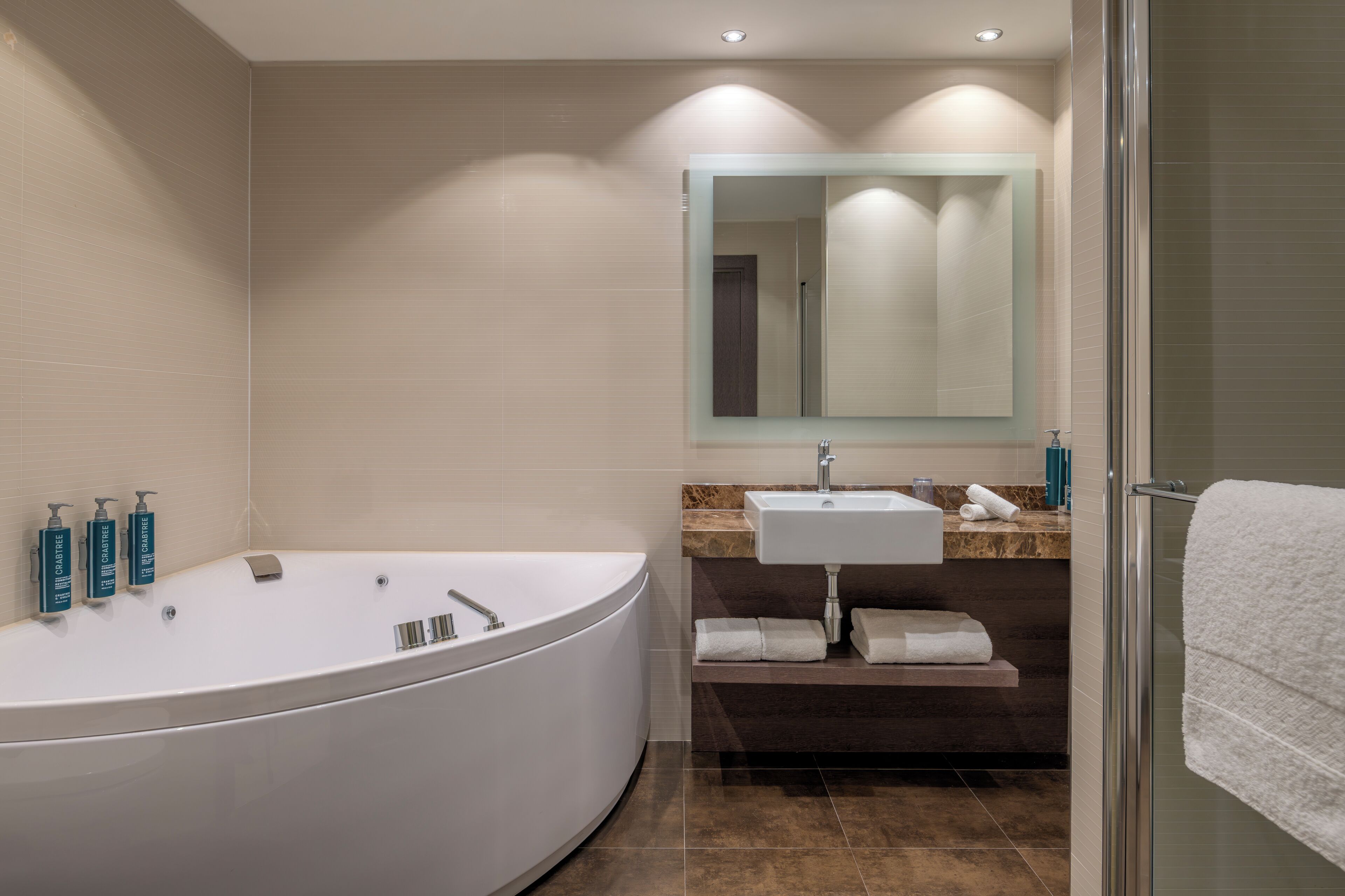 Ein modernes Badezimmer mit einer großen Badewanne, einem Waschbecken, einem Spiegel und Pflegeprodukten.