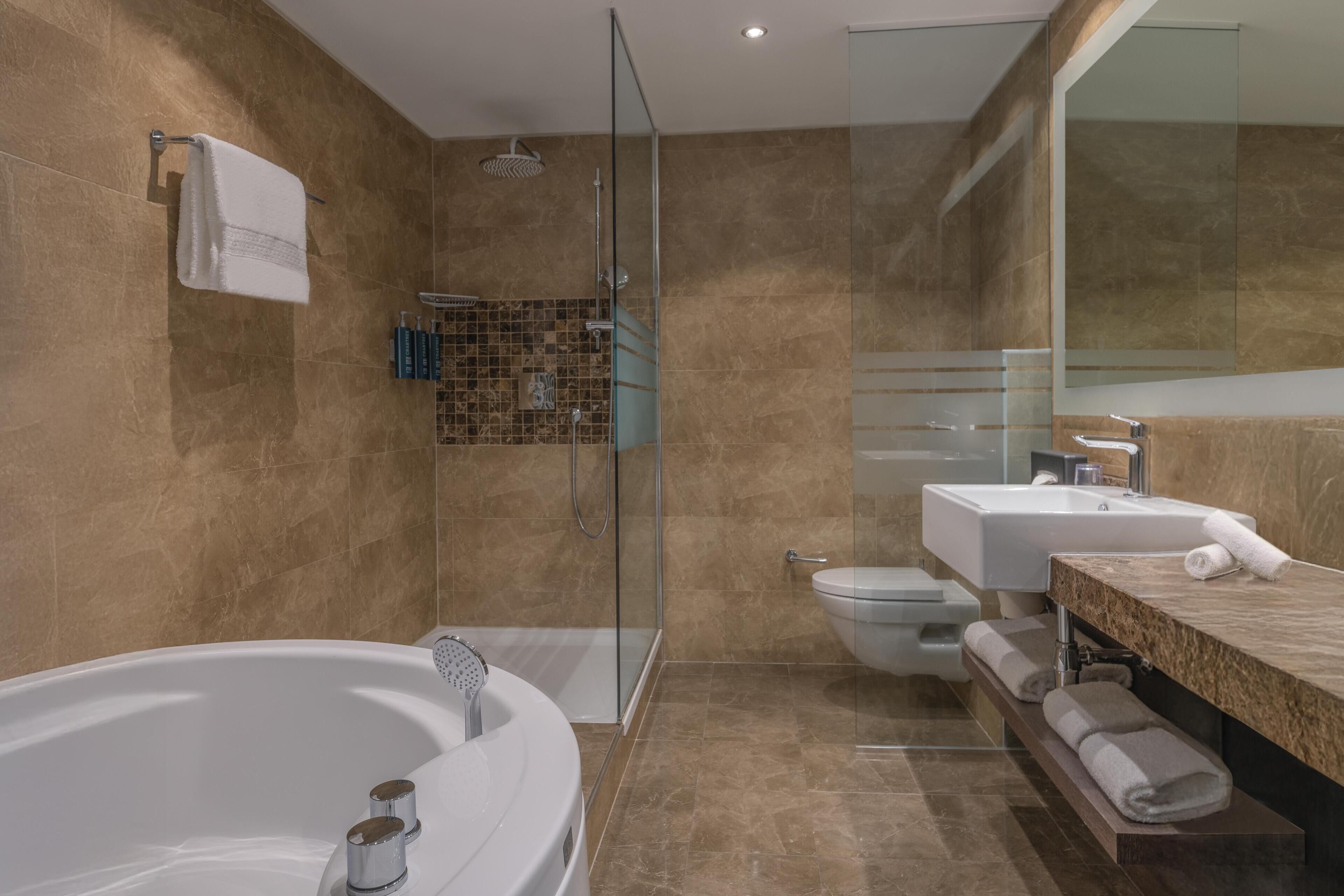 Un baño moderno con ducha envuelta en vidrio, una bañera independiente, un inodoro y un tocador con espejo.
