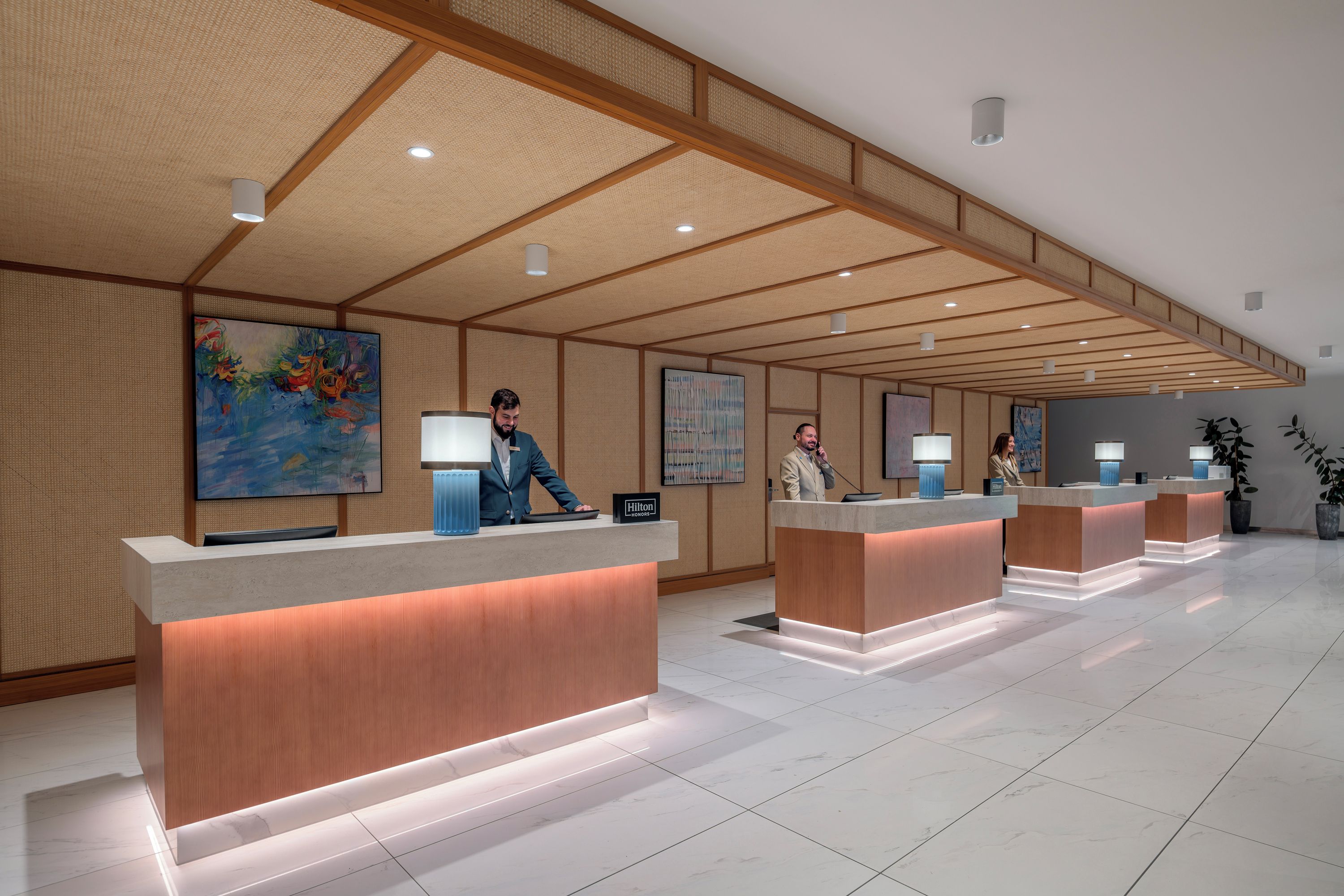 A hotel reception area with multiple counters, a high ceiling with wooden beams, and artwork on the walls.