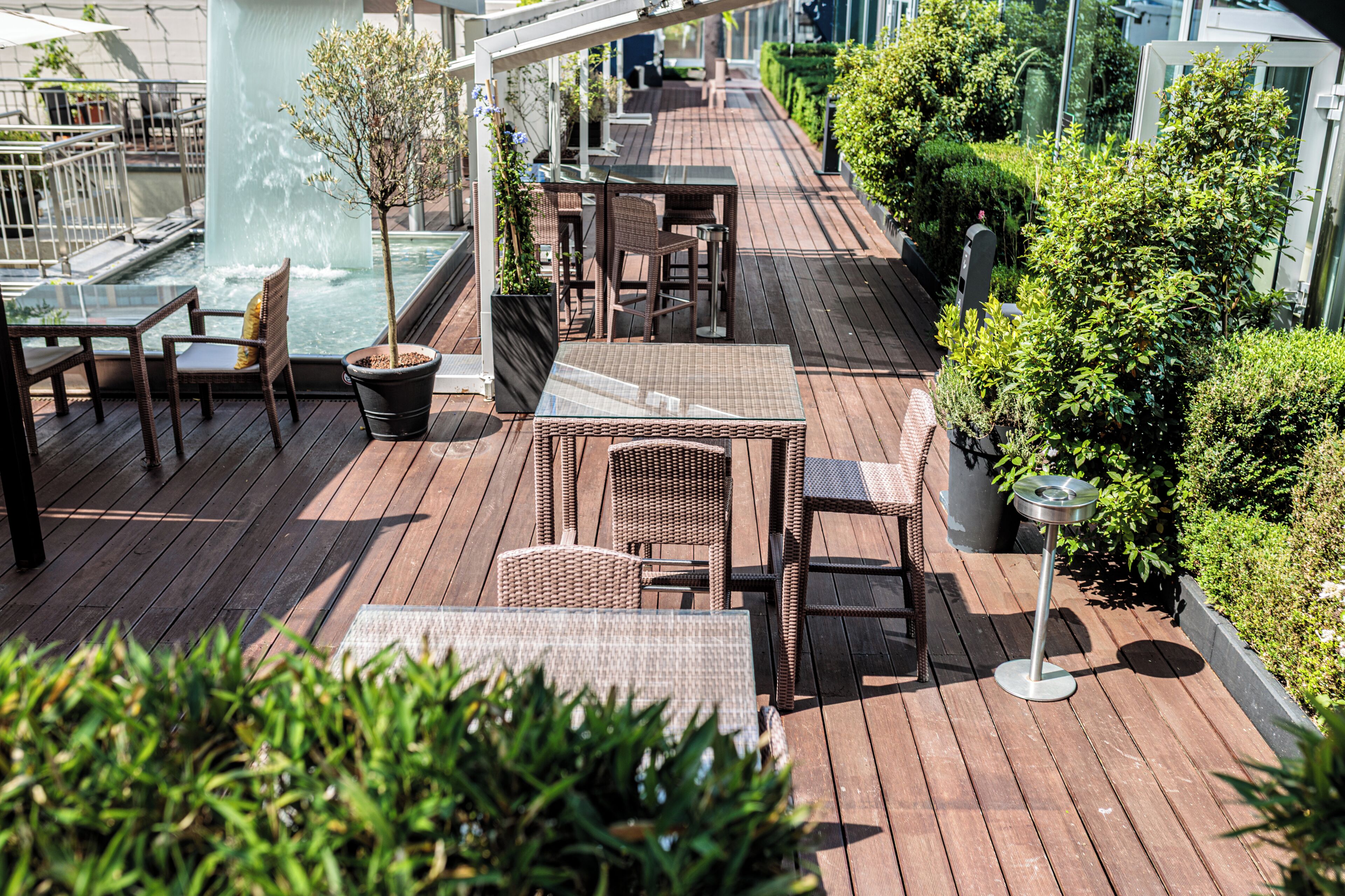 A wooden deck with outdoor furniture, a water feature, and greenery.