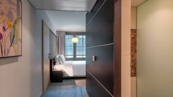 A hotel corridor with a bed, a nightstand, a lamp, and a painting on the wall.