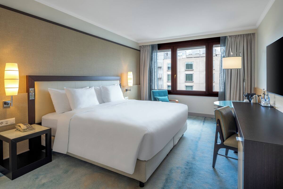 A hotel room with a large bed, bedside lamps, a desk, and a chair.