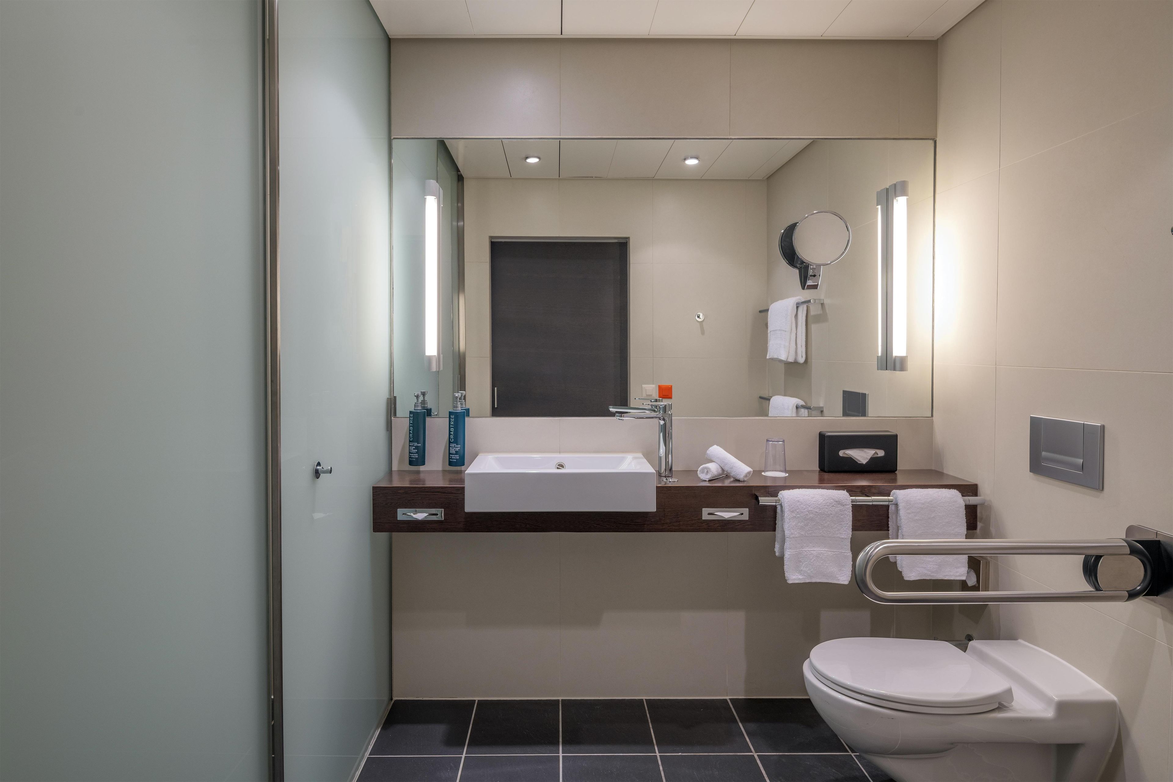 A modern bathroom with a white sink, a mirror, a toilet, and a towel rack.