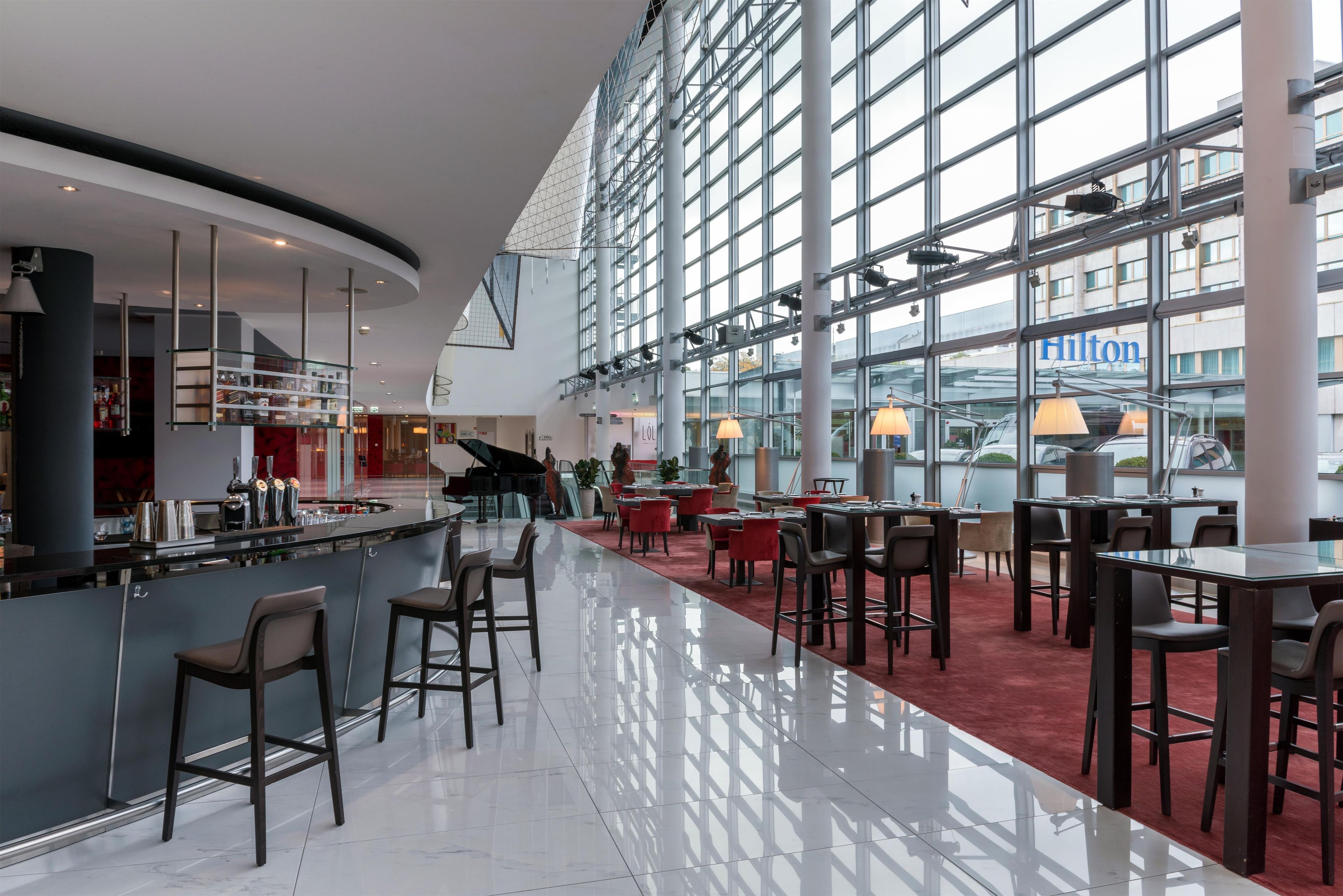 A spacious hotel lobby with a bar area, seating arrangements, and large windows offering views of the outside.