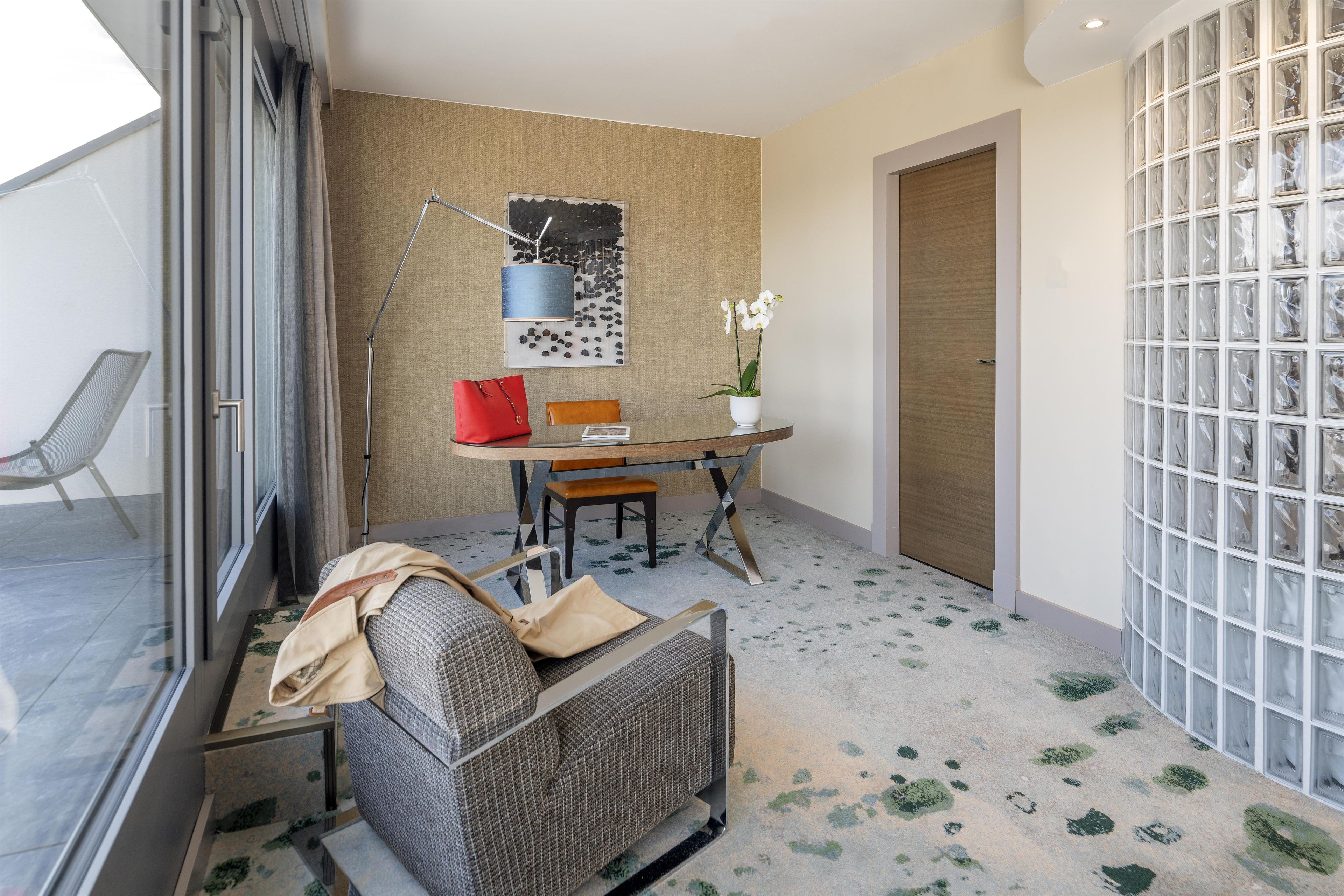 A modern room with a glass door, a dining table with chairs, a sofa, and a potted orchid.