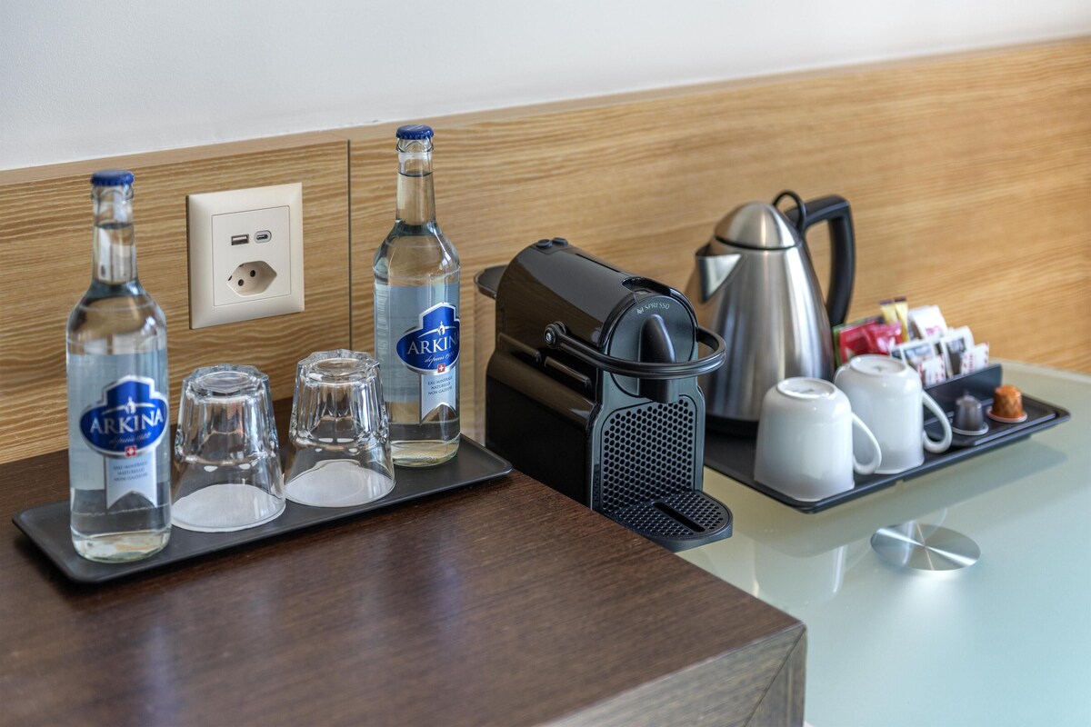 A hotel room's breakfast setup with a coffee maker, tea pots, a tray with pastries, and two bottles of water.