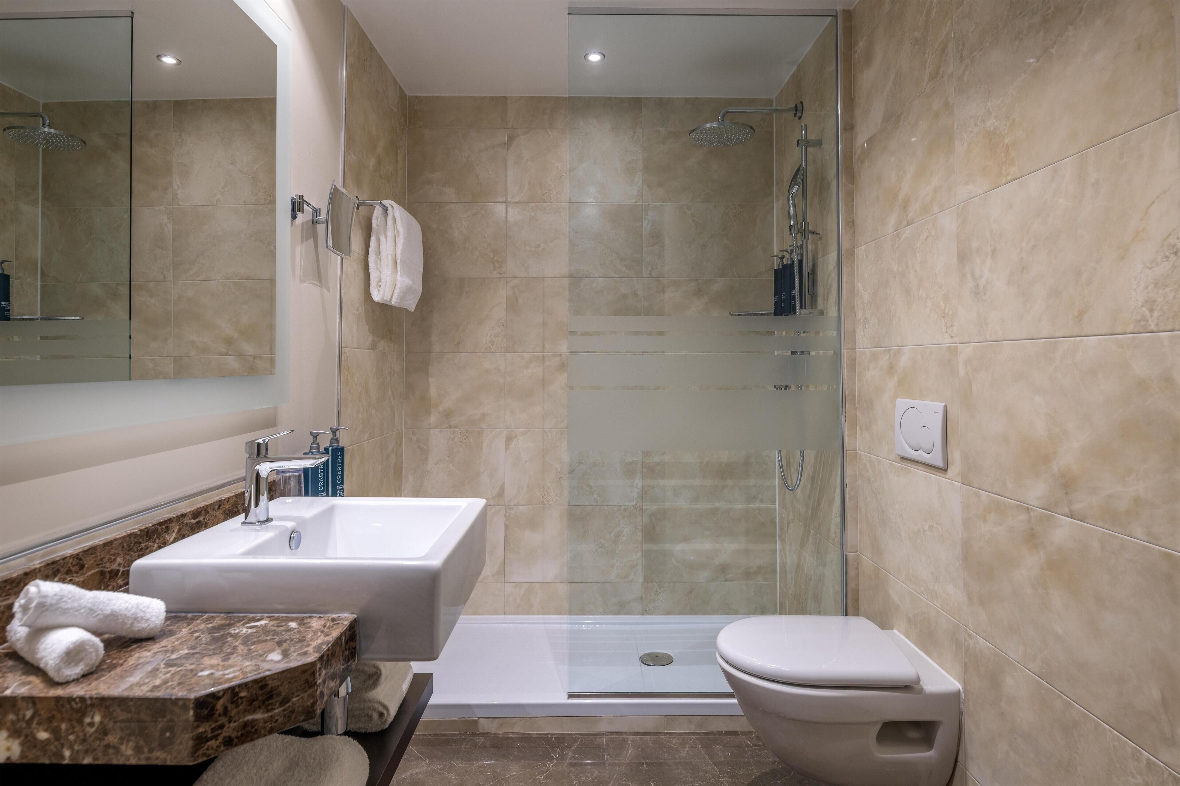 Un bagno moderno con doccia vetro, WC sospeso e lavabo su un mobile in marmo.
