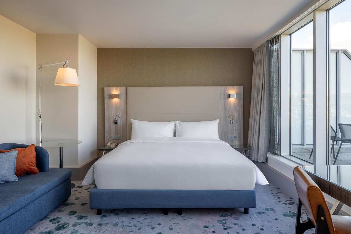 Ein Hotelzimmer mit einem großen Bett, einer Sitzecke, einem Schreibtisch und einem Fenster mit Blick.