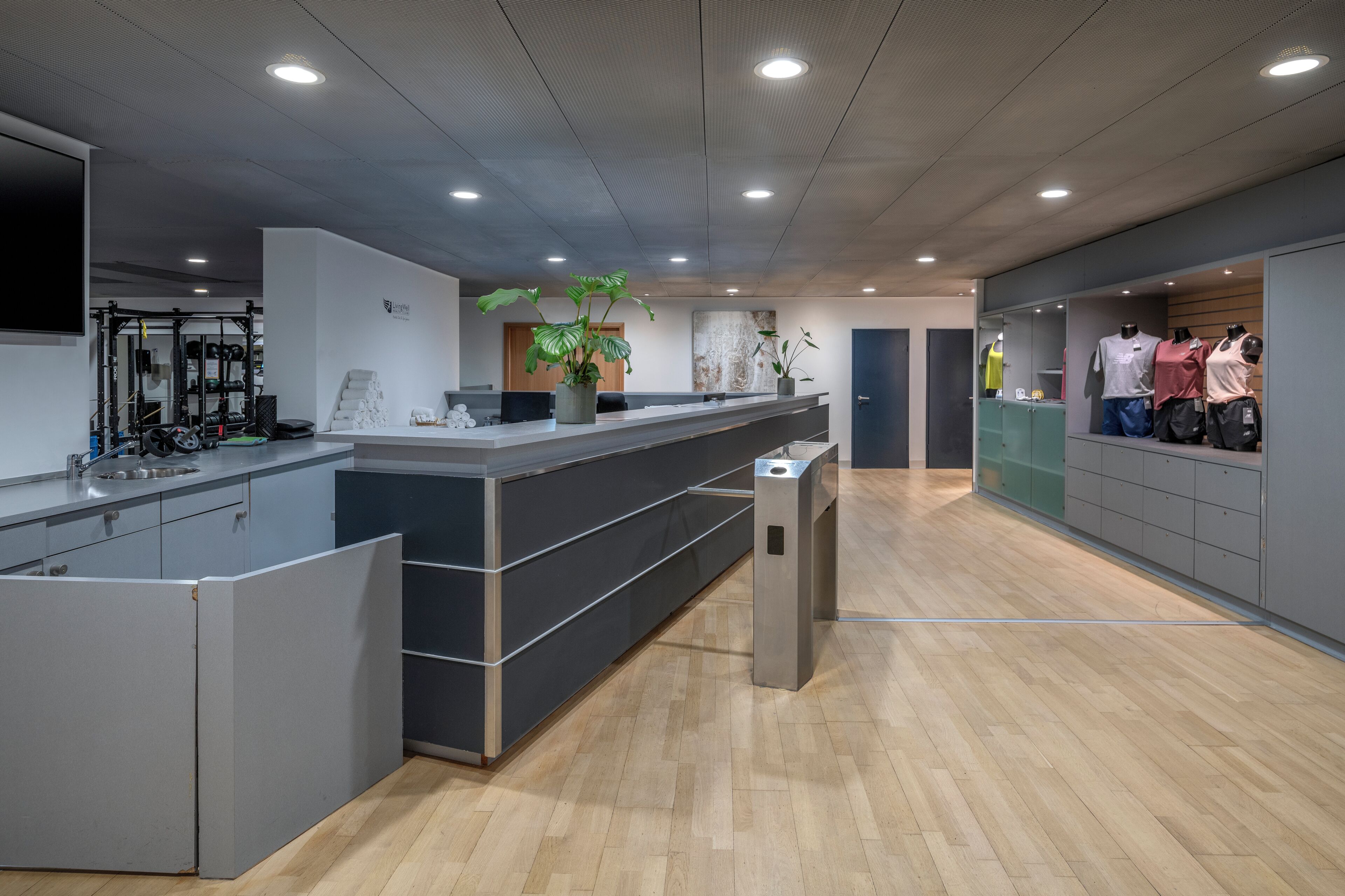 Un área de recepción moderna con una mesa de recepción, una planta y una exhibición de ropa informal.