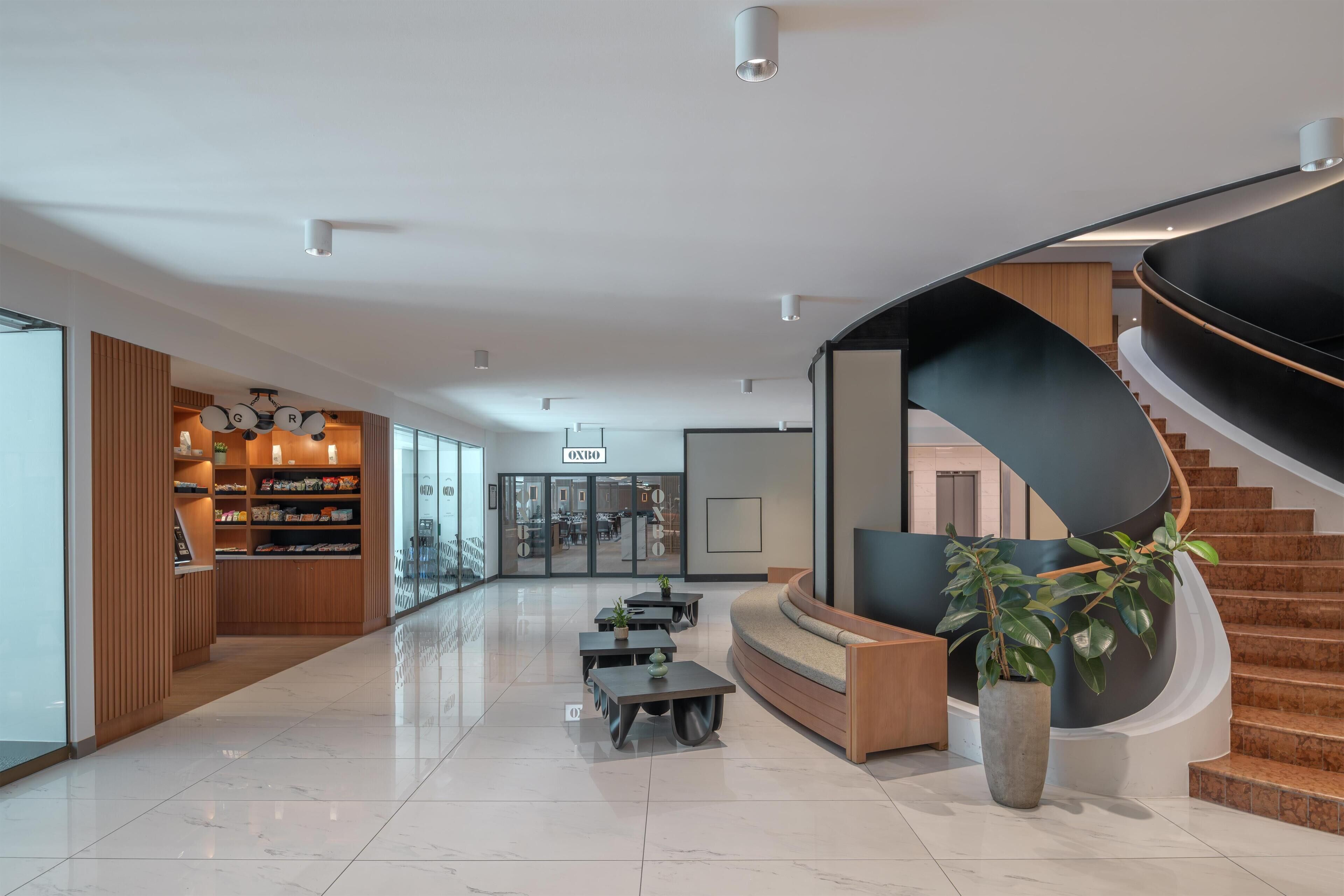 Un interior moderno con una escalera curva, una zona de recepción y un área de estar con mesas y sillas.