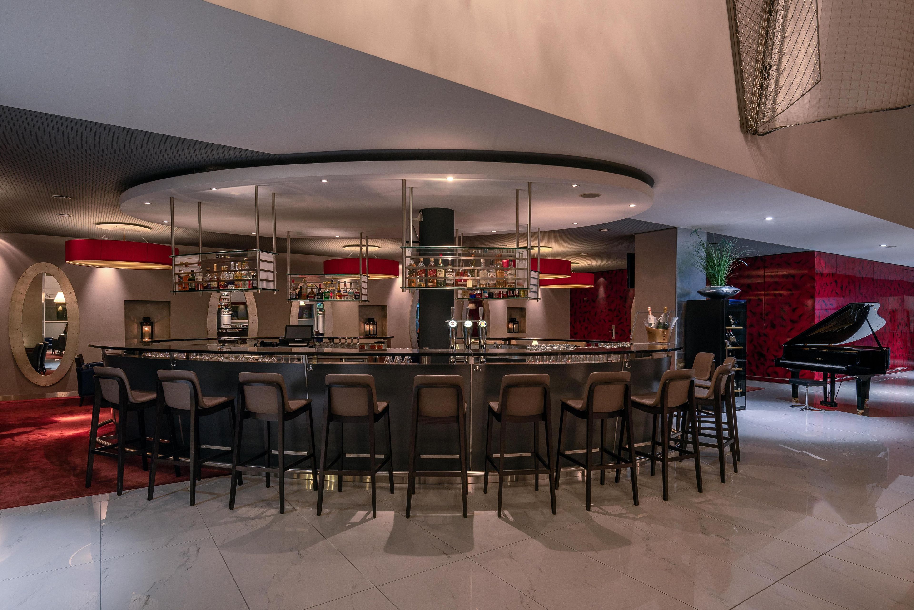 Un área de bar moderna con un diseño curvo, diversas opciones de asientos y un piano de cola al fondo.