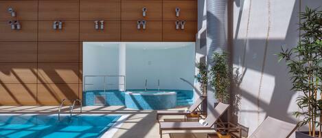Un área de piscina interior moderna con sillones de descanso, un jacuzzi y plantas de bambú.