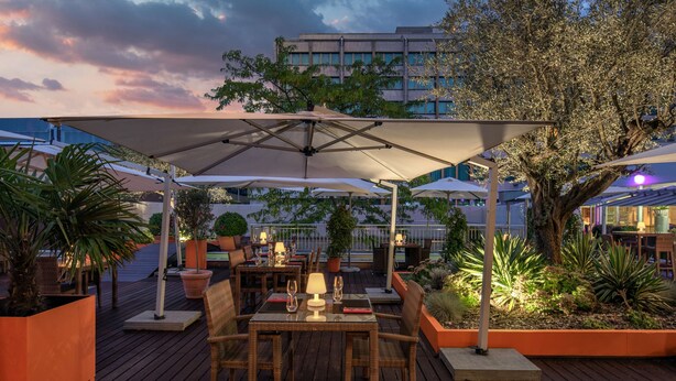 A wooden deck with outdoor seating, umbrellas, and potted plants. - Hilton Geneva Hotel and Conference Centre (Le Grand-Saconnex)