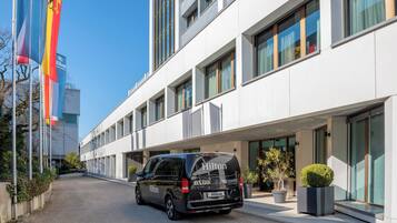 Een modern gebouw met een zwarte bestelwagen ervoor, vlaggen en een heldere lucht.