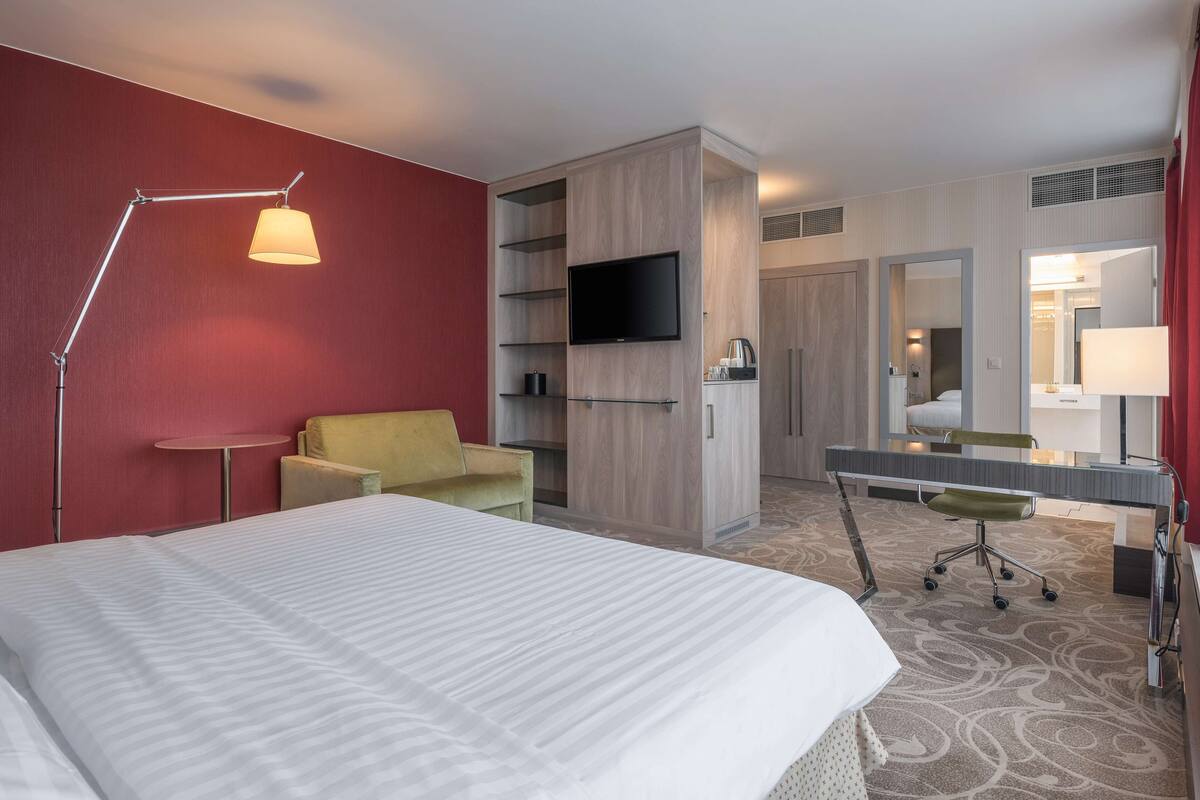A hotel room with a bed, a desk, a chair, a TV, and a mirror.