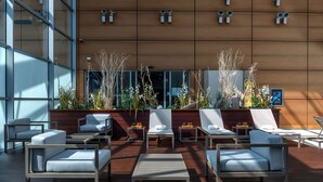 A modern outdoor seating area with lounge chairs and tables, a wooden wall with windows, and decorative plants. - Hilton Geneva Hotel and Conference Centre (Le Grand-Saconnex)