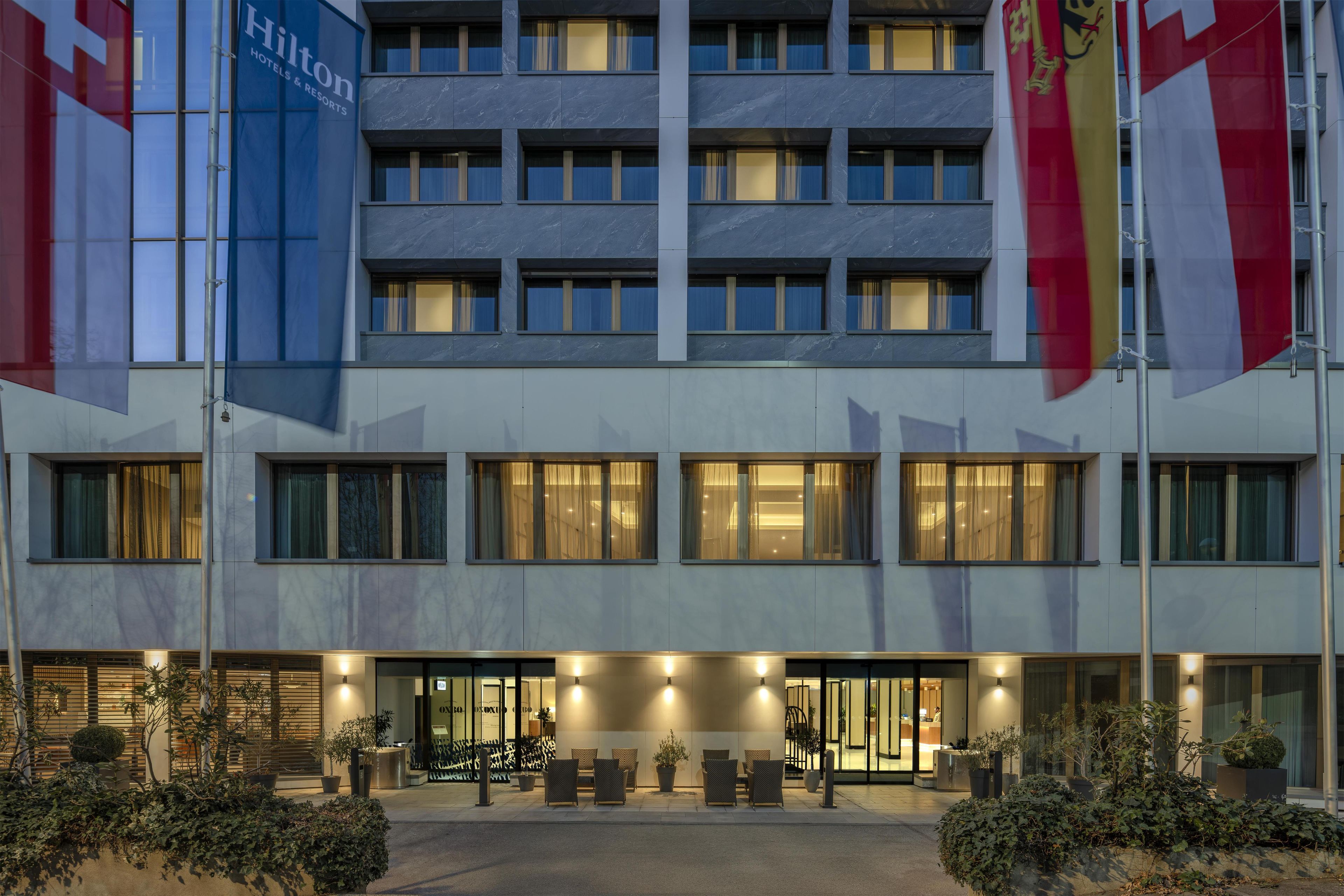 A modern hotel building with multiple floors, large windows, and a well-lit entrance area with seating.