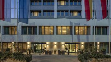 A modern hotel building with multiple floors, large windows, and a well-lit entrance area with seating.