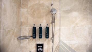 A bathroom with a shower, a hand dryer, and three bottles of Crabtree shampoo.