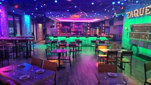 A restaurant with multiple tables and chairs, a bar area, and a neon sign on the wall. - Holiday Inn & Suites Parsippany Fairfield by IHG (Parsippany)
