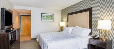 A hotel room with a bed, bedside lamps, a television, and a door leading to another room.