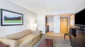 Habitación de hotel con sofá, una mesita, televisor, lámpara y un cuadro en la pared.