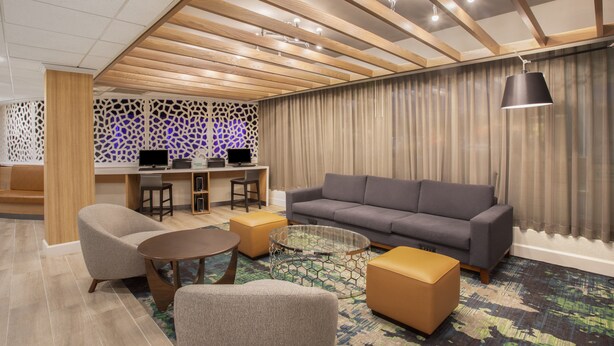 Un área de descanso moderna con sofá, sillones, una mesa de centro y un escritorio con computadoras.